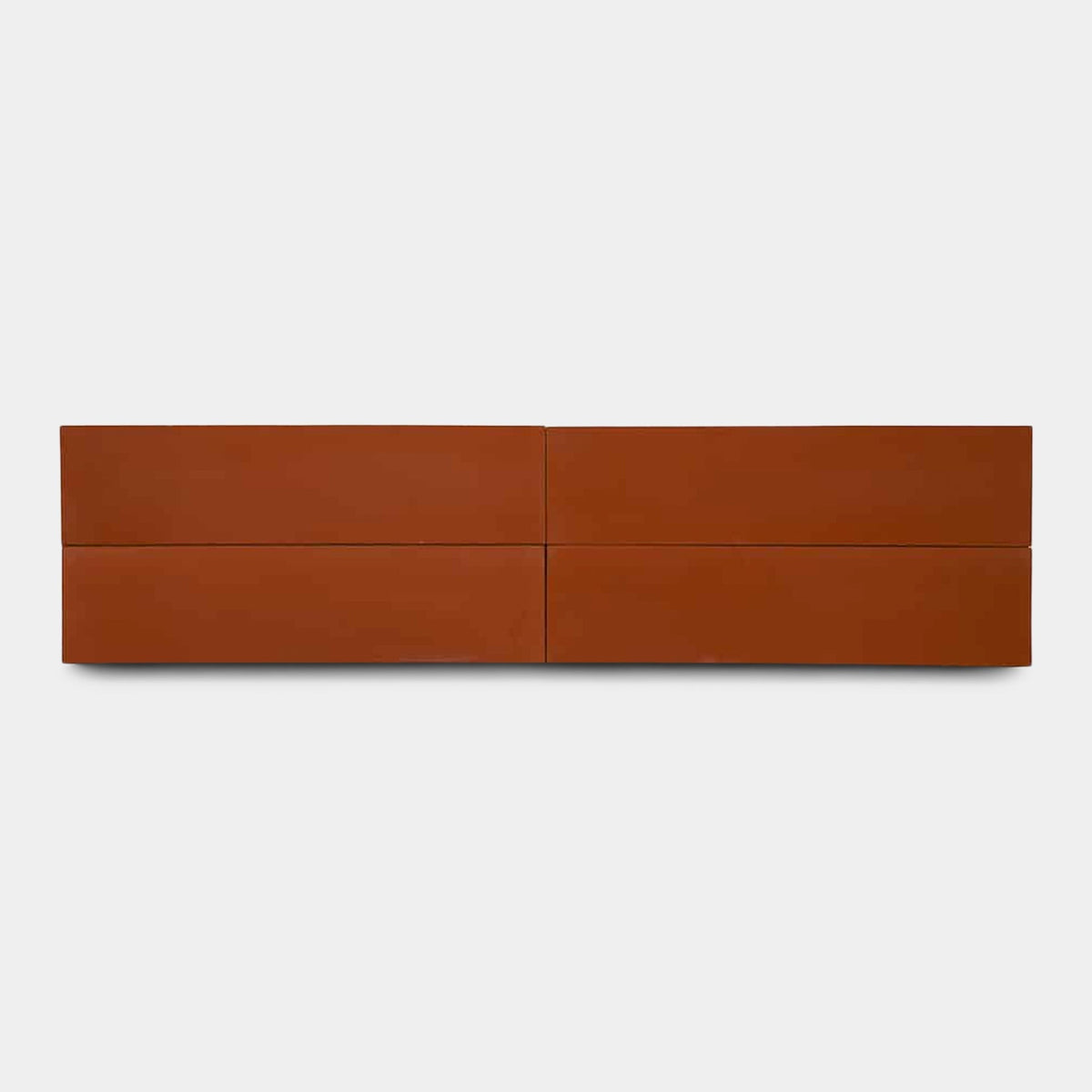 A minimalist, wall-mounted, four-drawer dresser in matte burnt orange evokes the warmth of Zia Tile’s Atomic 2x8, Sample ceramic tile, shown against a plain white background.