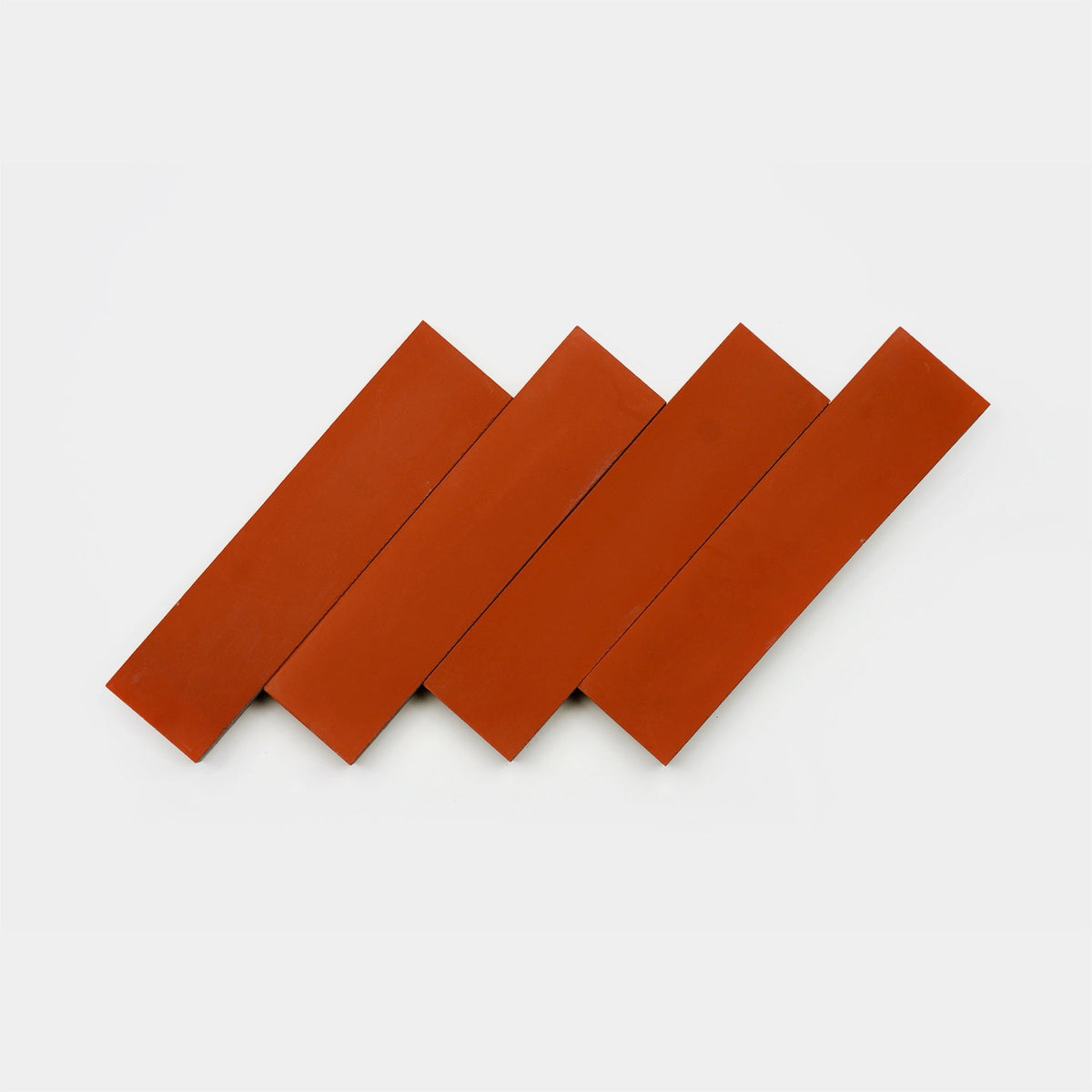 Four red Atomic 2x8 ceramic tile samples by Zia Tile are arranged diagonally and overlapping on a plain white background, forming a zigzag pattern.