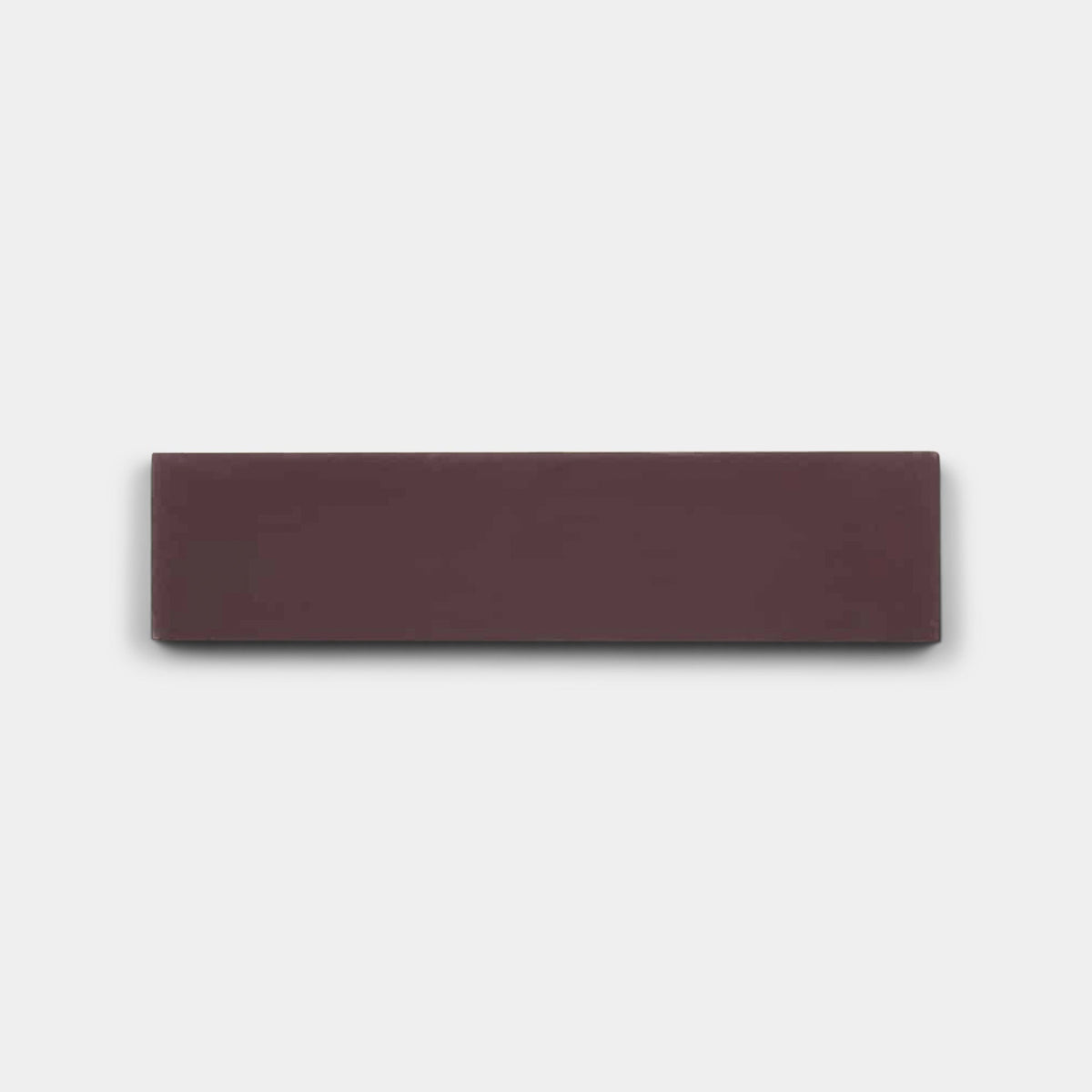 A rectangular, dark brown eraser is centered on a plain, light gray background, evoking the rich tones of Zia Tile’s Aubergine 2x8 sample.