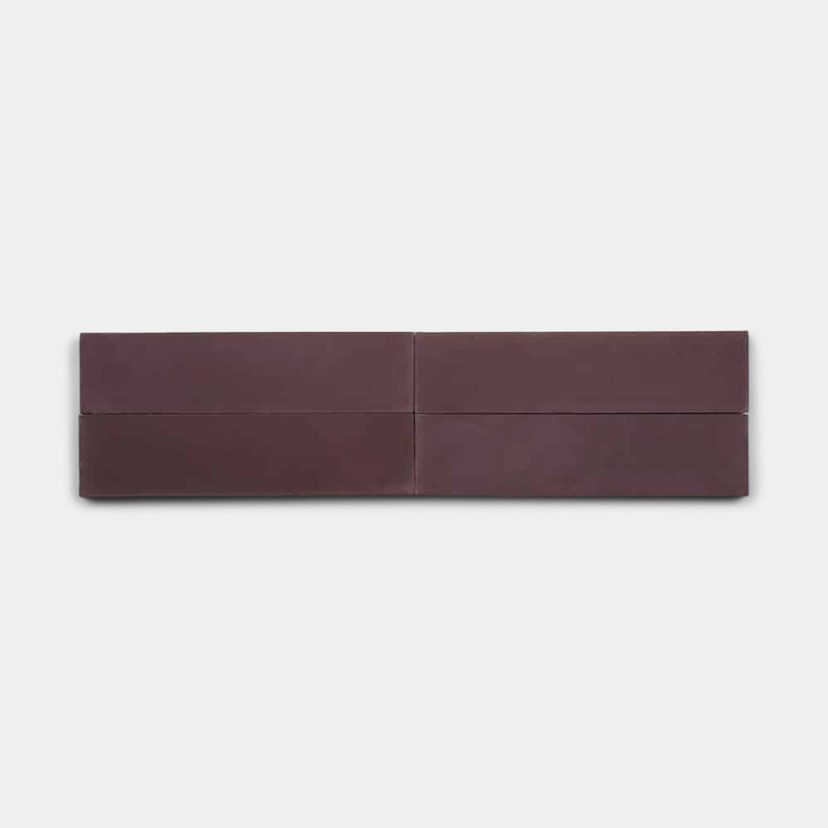 A minimalist image featuring four Zia Tile Aubergine 2x8 samples, all dark brown rectangles, arranged in a horizontal row on a plain light gray background.