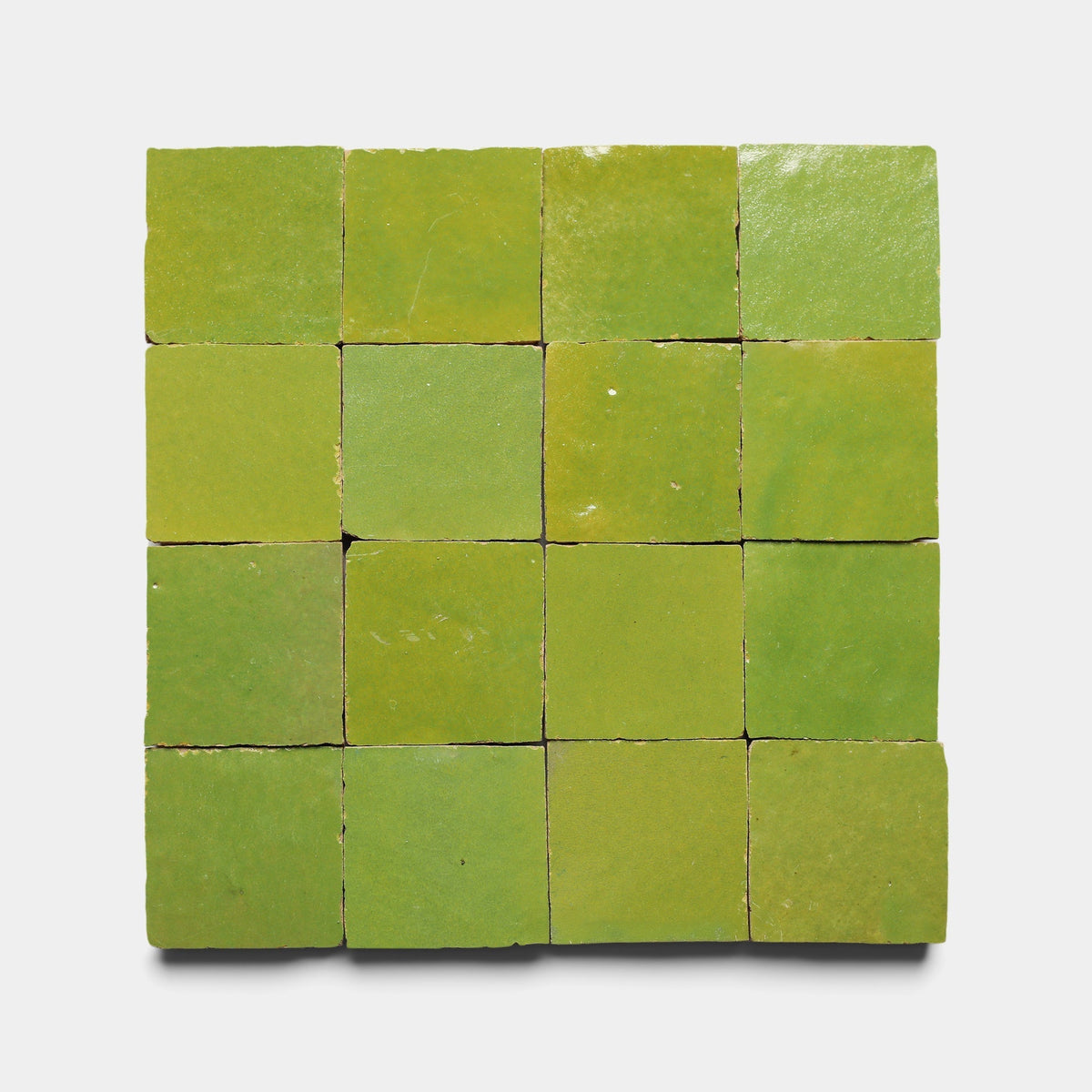A 4x4 grid of Zia Tile’s Avocado 2x2, Sample green ceramic tiles, each with subtle shade variations and a glossy finish, arranged on a plain white background.