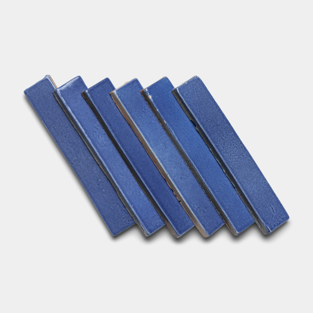 Six Azul Mini Bar tiles by Zia Tile, in rectangular blue ceramic, are arranged in a slightly diagonal, overlapping pattern on a white background.