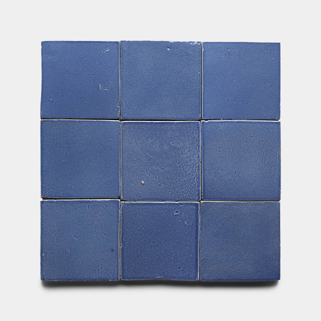 Nine Azul 4x4 Square tiles by Zia Tile, featuring a matte blue finish and unique Cotto imperfections, are arranged in a 3x3 grid on a white background. Each ceramic tile shows slight texture variations for a handmade look.
