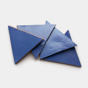 Four glossy Azul Triangle tiles from Zia Tile, in blue ceramic, are arranged in a slightly overlapping, scattered pattern on a white background.