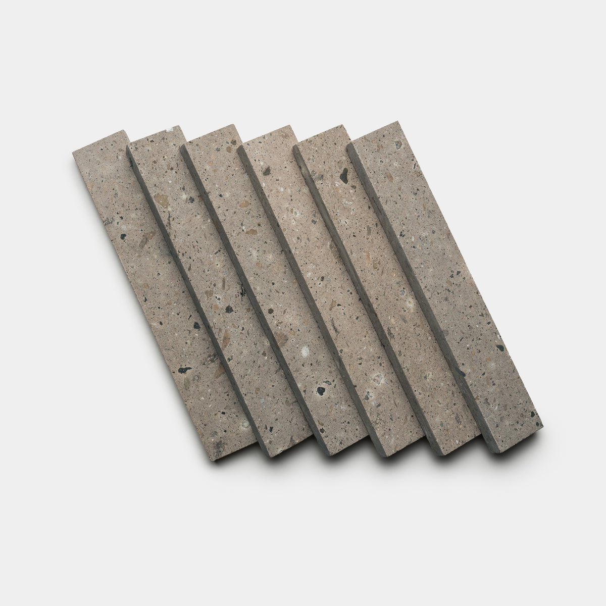 Six Badlands 2x12 terrazzo tiles by Zia Tile are arranged in a slightly fanned-out pattern on a white background, showcasing their neutral, speckled surface with small colorful chips.