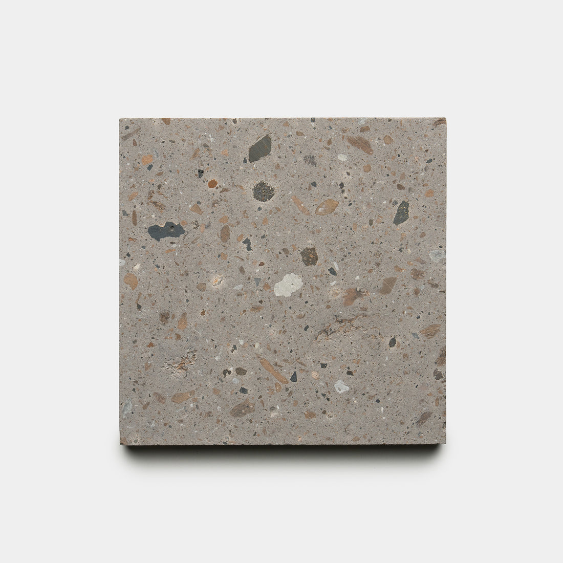 The Badlands 6x6 by Zia Tile is a square terrazzo tile featuring a gray base with beige, brown, black, and white chips of varying sizes, shown on a plain white background.