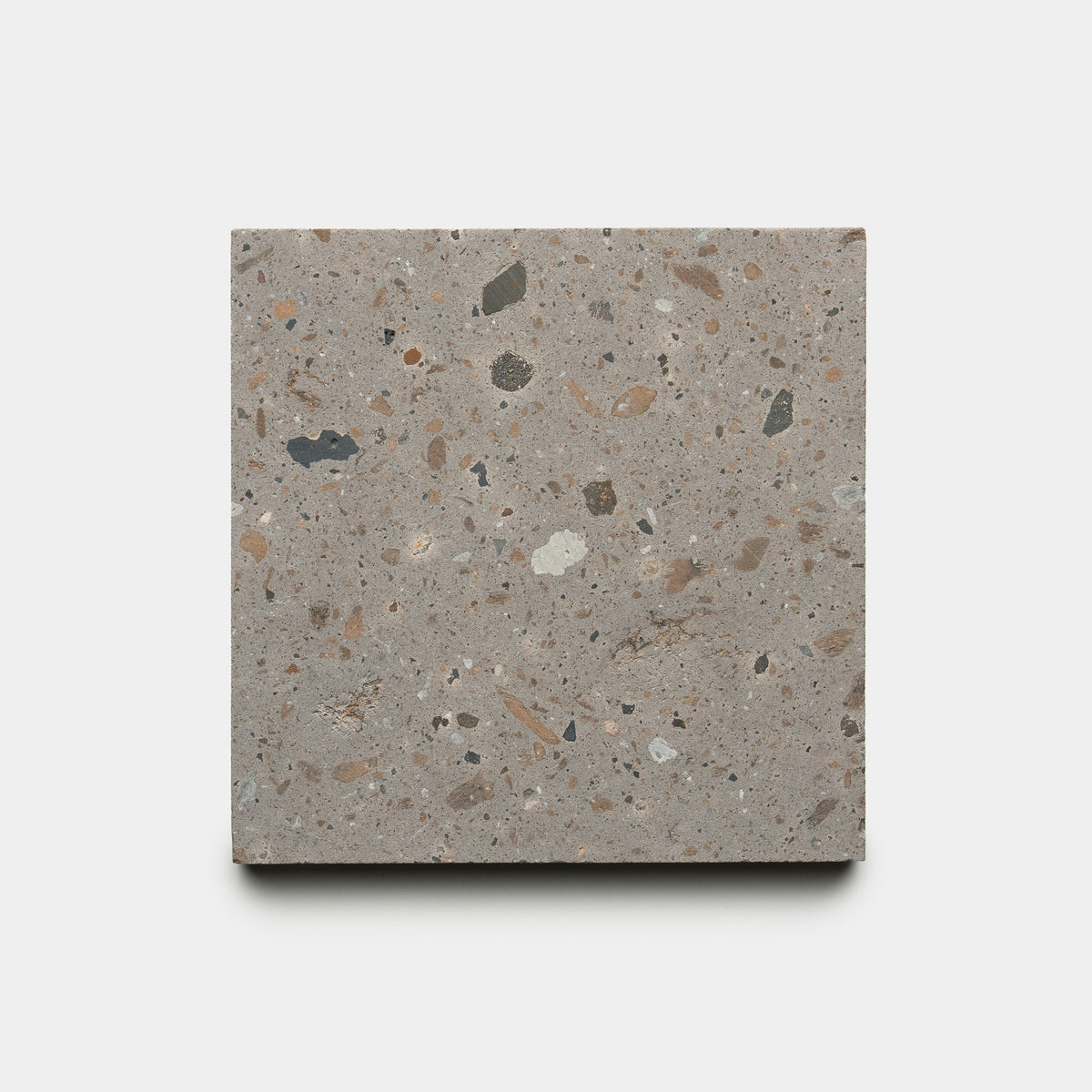 The Badlands 6x6 by Zia Tile is a square terrazzo tile featuring a gray base with beige, brown, black, and white chips of varying sizes, shown on a plain white background.