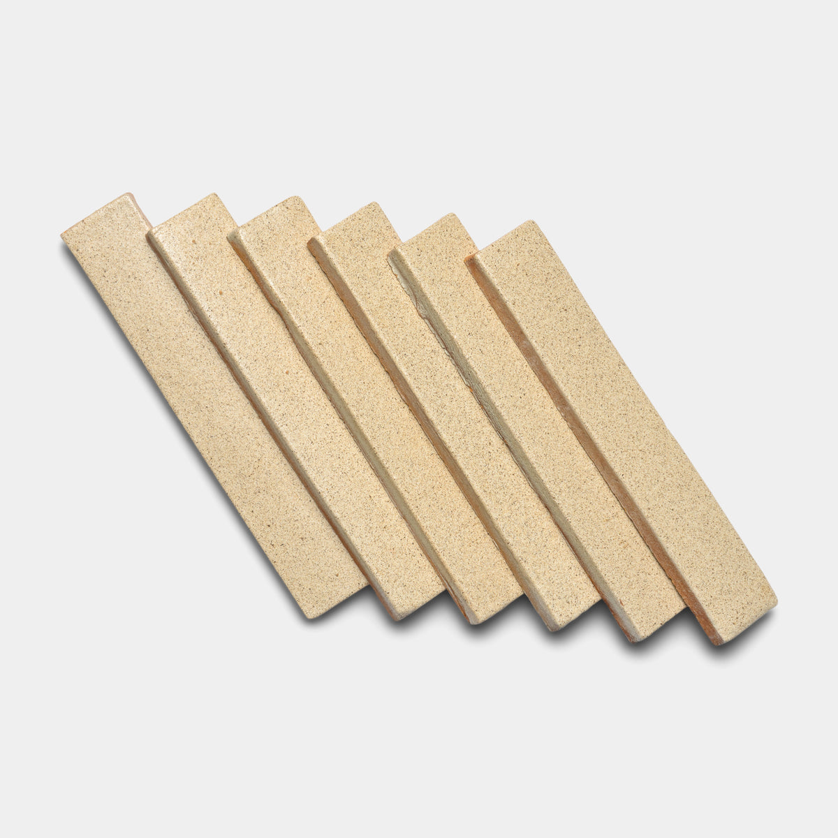 Six Baja Mini Bar tiles by Zia Tile, in a rectangular beige design, are arranged diagonally in a row on a white background with slight overlap.