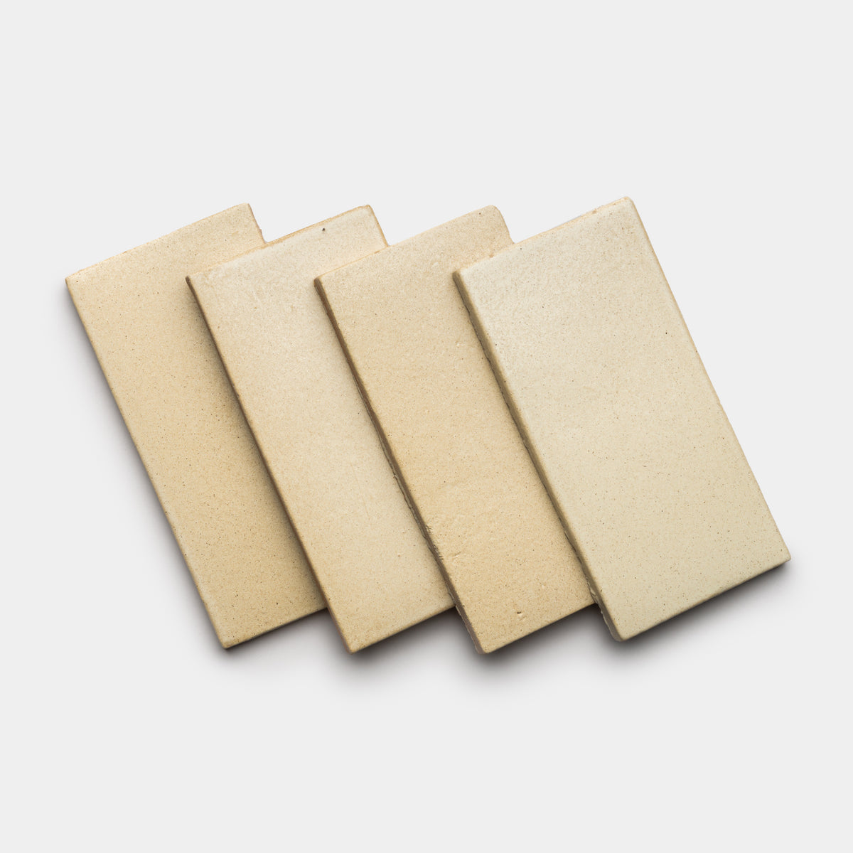 Four Baja 4x8 Rectangle tiles by Zia Tile in beige ceramic are arranged in a slightly overlapping diagonal row on a white background.