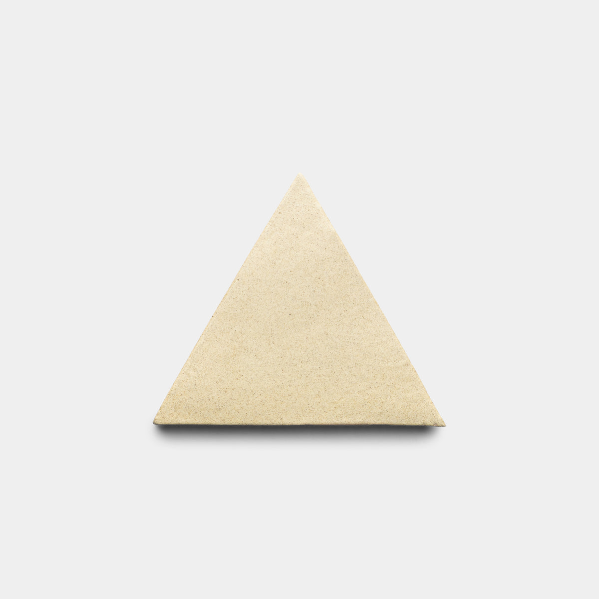 The Zia Tile Baja Triangle, a smooth and matte beige tile, is centered on a light gray background. The triangular tile has no visible markings or texture.