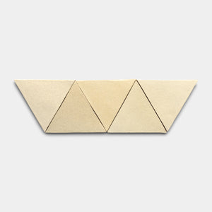 Six Baja Triangle tiles by Zia Tile, in beige, are arranged side by side in a horizontal row to create a zigzag pattern against a plain light gray background.