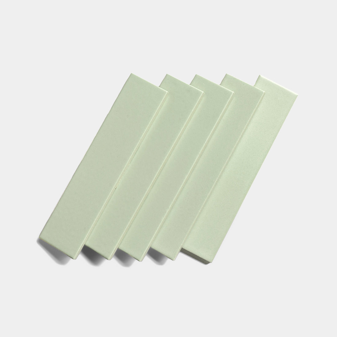 Five Balsam 2x8 ceramic tiles by Zia Tile, featuring a light green matte finish, are arranged in a slightly overlapping diagonal row against a plain white background.