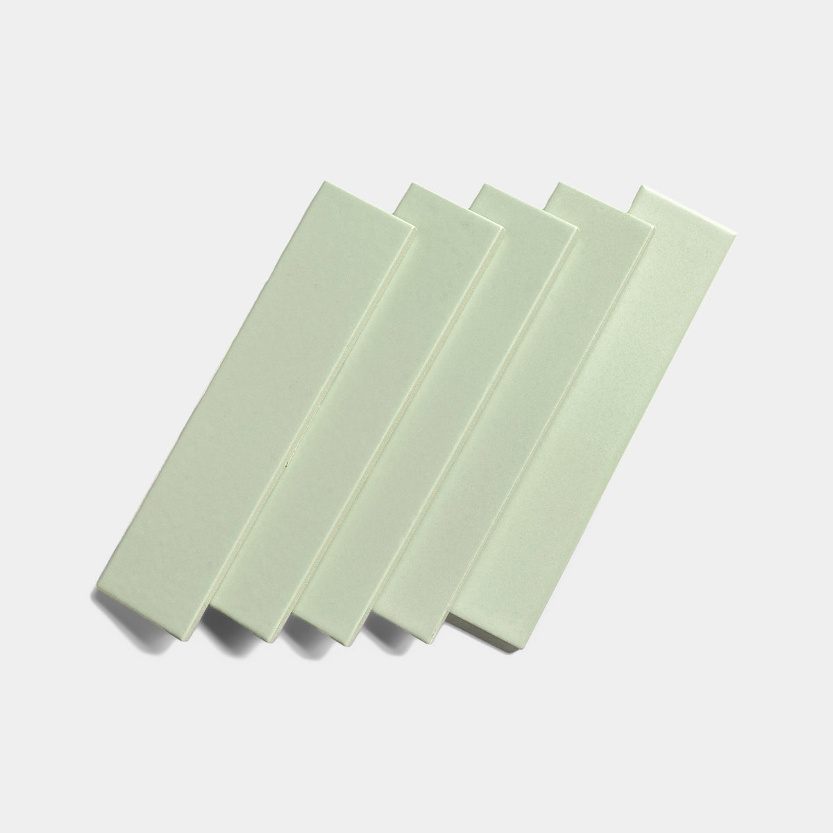 Five Balsam 2x8 ceramic tiles by Zia Tile, featuring a light green matte finish, are arranged in a slightly overlapping diagonal row against a plain white background.