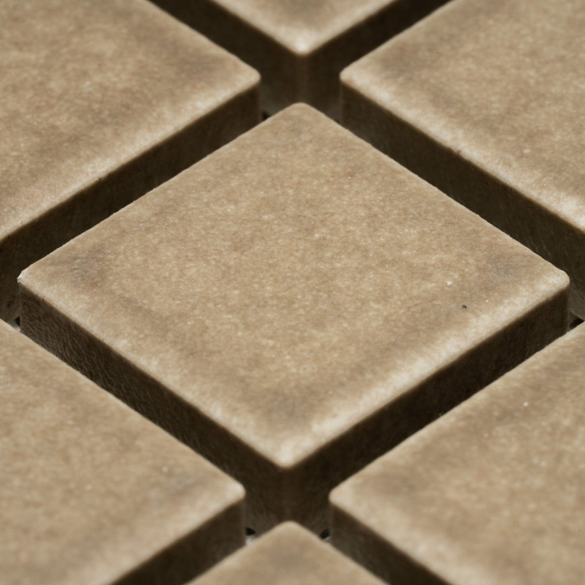 Close-up of Zia Tile's Barley 1x1: several raised, square brown tiles in a grid. The tiles feature a smooth matte finish, soft edges, and visible shadows between each one.