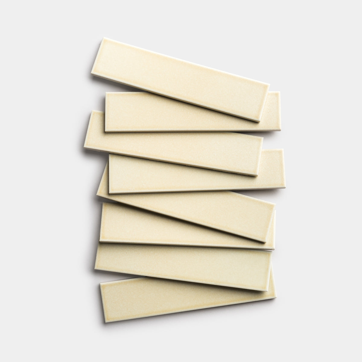 Eight Birch 2x8 rectangular tiles by Zia Tile, in a cream tone, are stacked in a slightly uneven, overlapping layout on a plain light gray background.