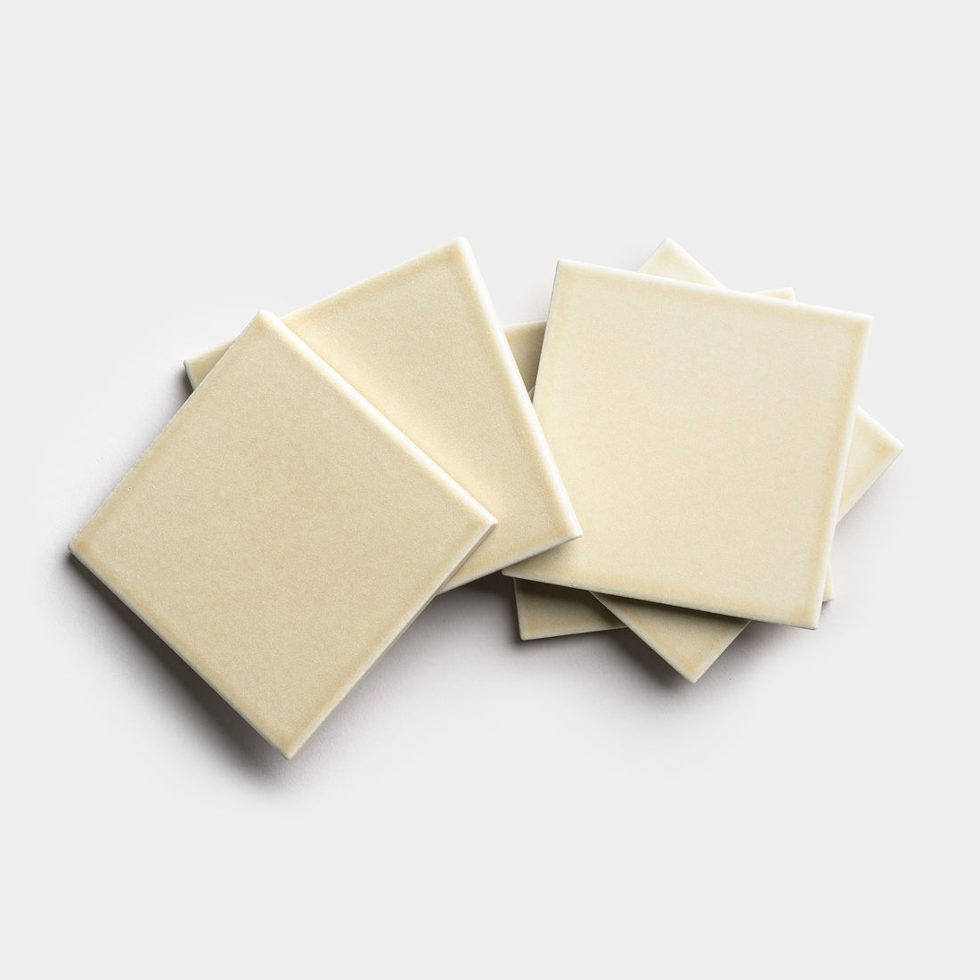 Six Birch 4x4 beige square ceramic tiles by Zia Tile are arranged in a slightly overlapping, scattered pile on a plain white background.
