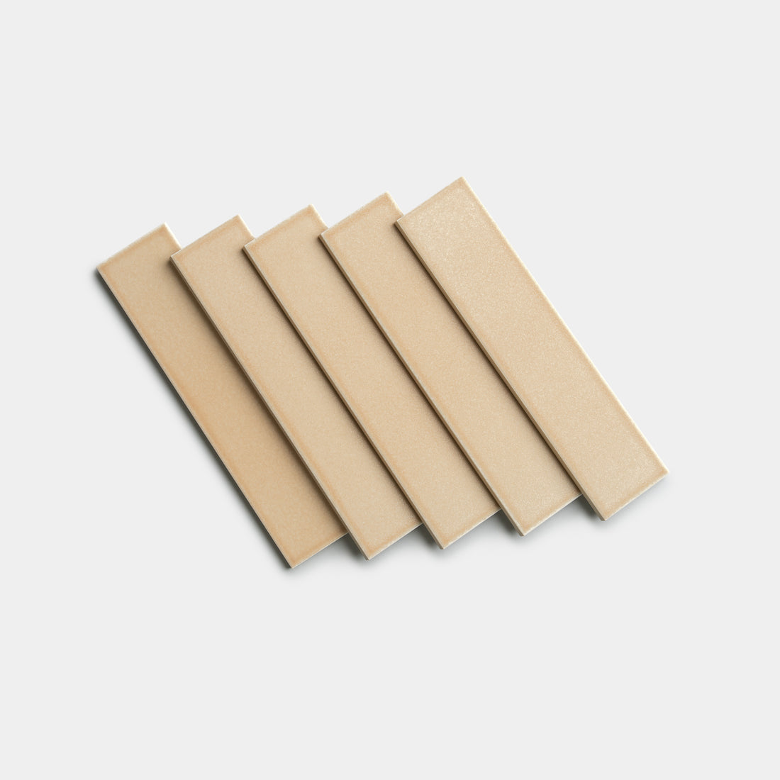 Five Zia Tile Biscuit 2x8 rectangular beige tiles are arranged diagonally in a staggered, overlapping pattern on a plain white background.