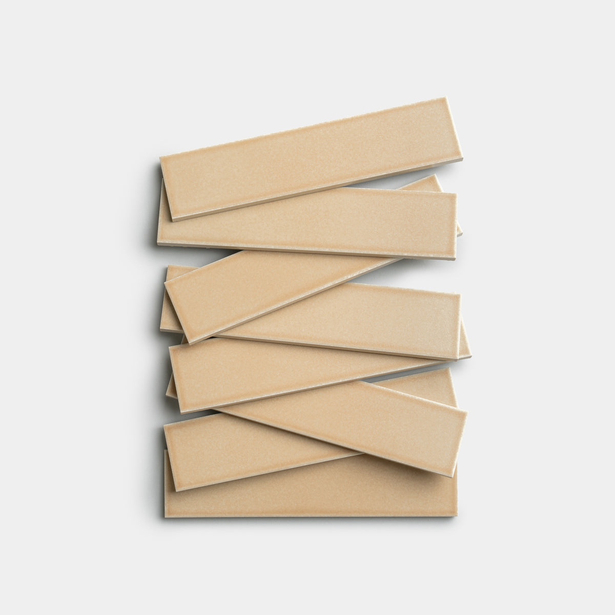 Six Zia Tile Biscuit 2x8 rectangular beige tiles are stacked in a staggered, crisscross pattern on a light gray background.