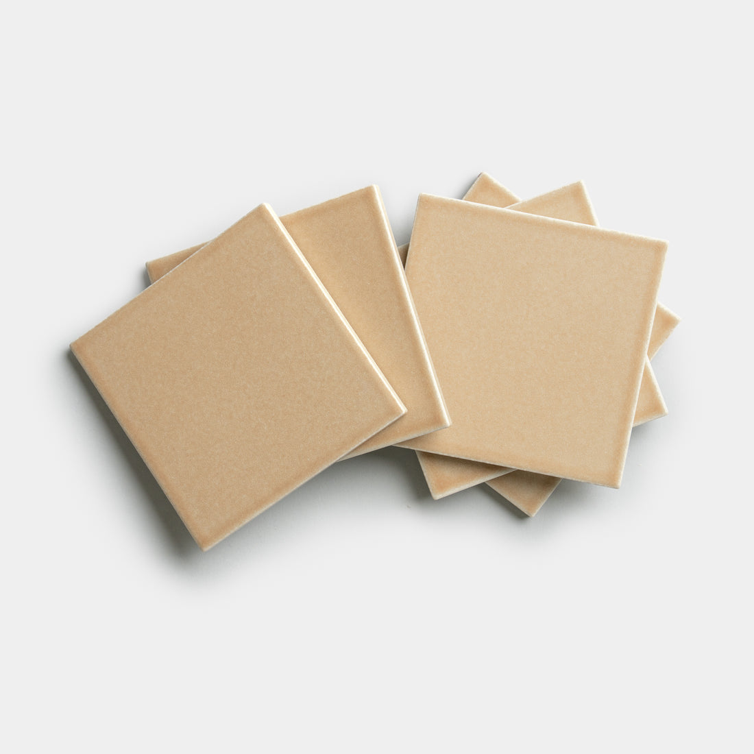 Five Biscuit 4x4 tiles by Zia Tile in beige ceramic are stacked in a slightly fanned arrangement on a plain white background.