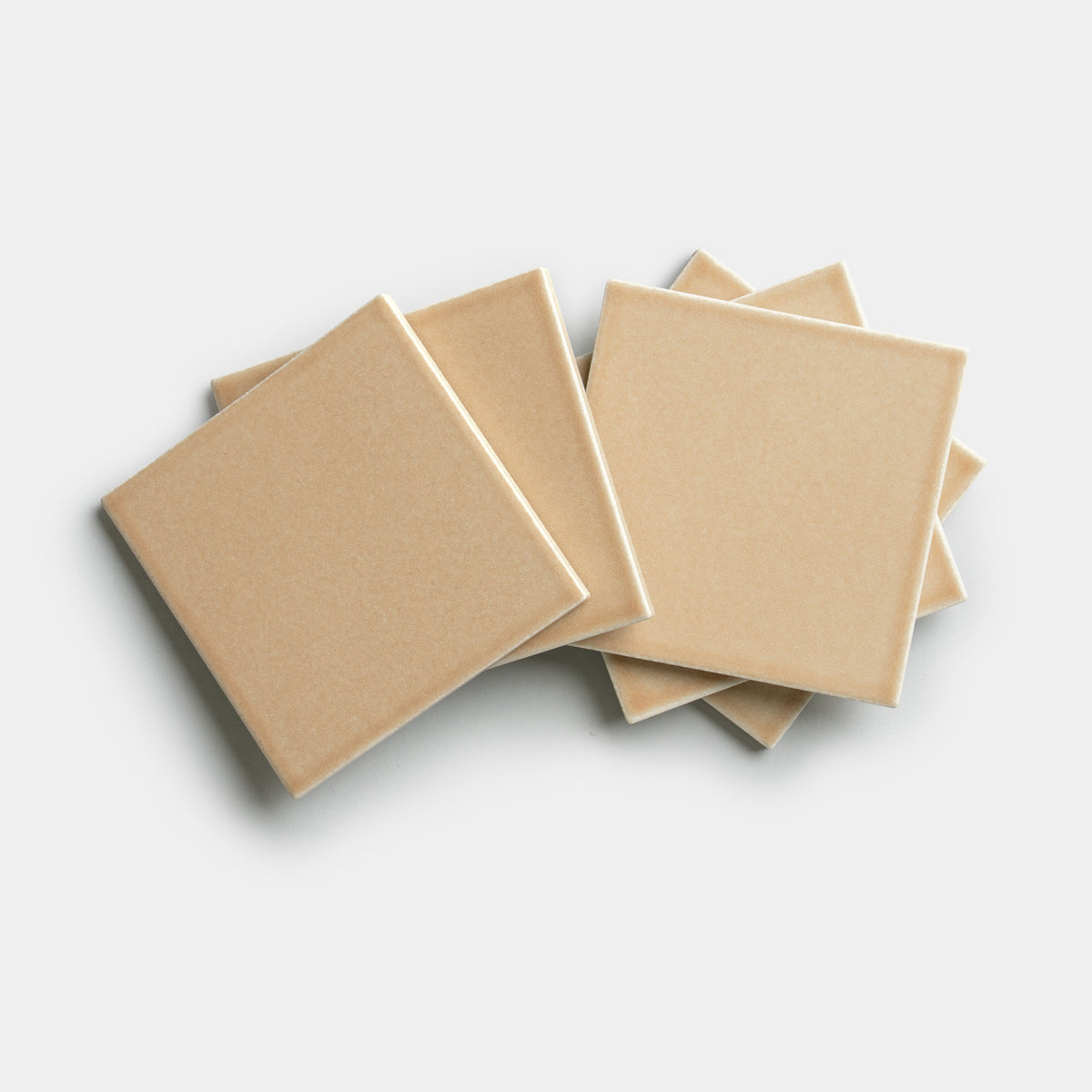 Five Biscuit 4x4 tiles by Zia Tile in beige ceramic are stacked in a slightly fanned arrangement on a plain white background.