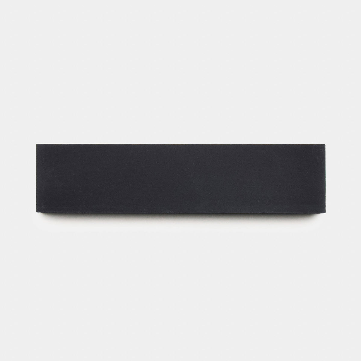 A Black 2x8, Sample by Zia Tile is centered on a plain white background, its clean lines echoing the distinctive handmade aesthetic of Zia Tile collections.