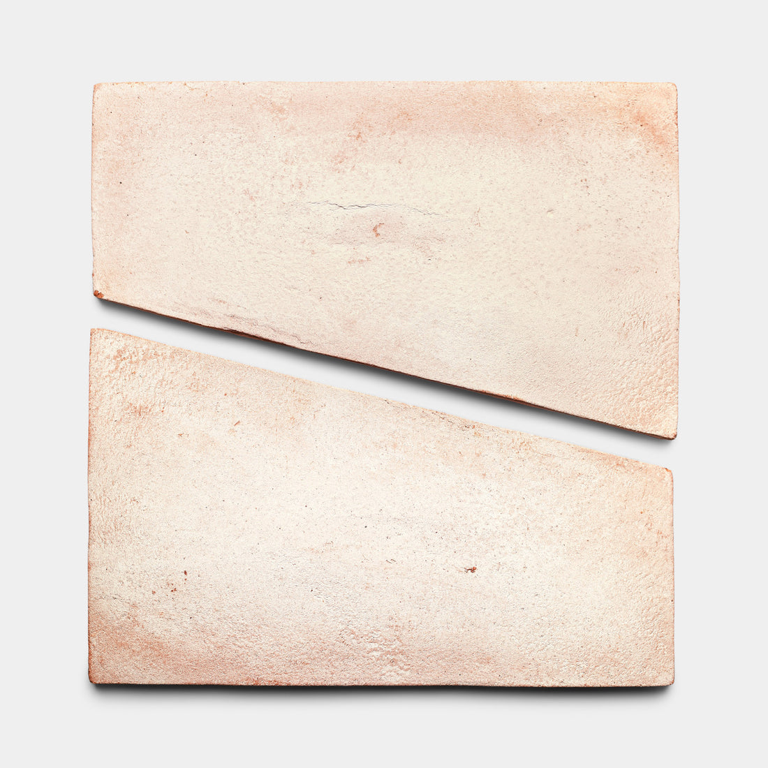 Two light brown Toltec + Blanco clay bricks from Zia Tile rest on a white background—one brick is diagonally split into two trapezoidal pieces, forming the original rectangle and highlighting ceramic craftsmanship.