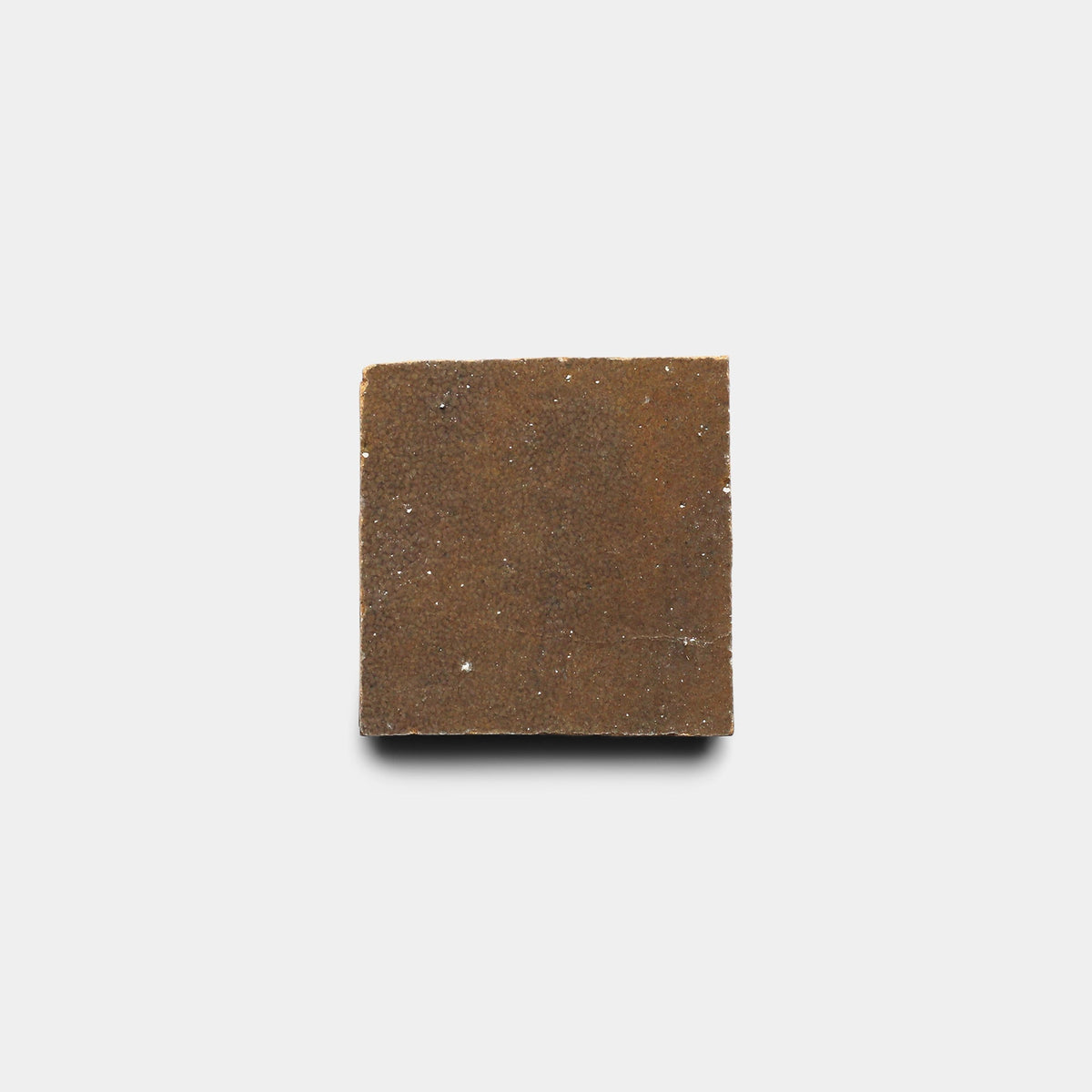 A Brownstone 2x2 sample from Zia Tile, featuring a handmade look with rough texture and brown color, sits on a plain white background.