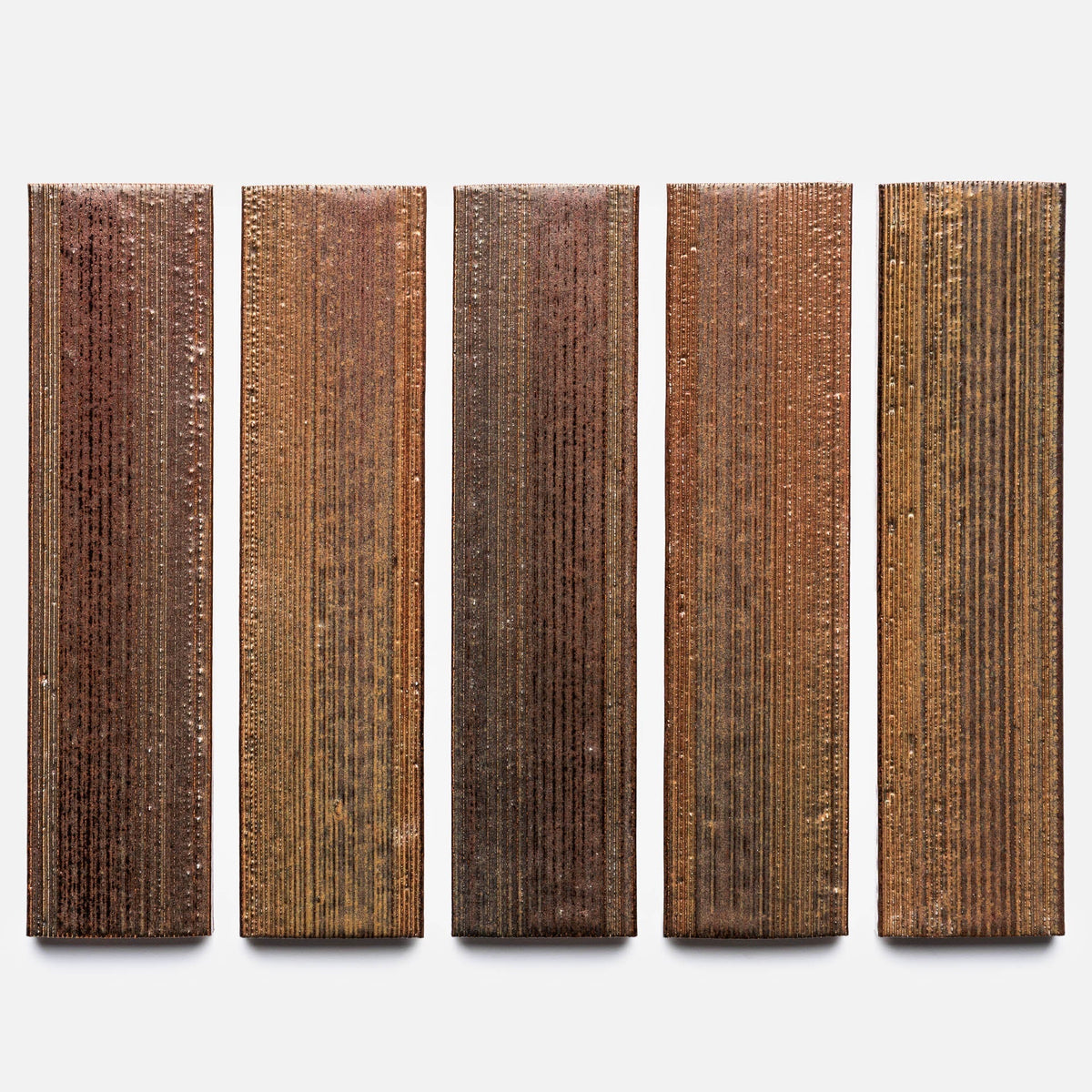 Five rectangular Buckeye + Etched ceramic tile samples by Zia Tile, each in varying brown and copper shades with a textured linear pattern, are evenly spaced vertically against a plain white background.
