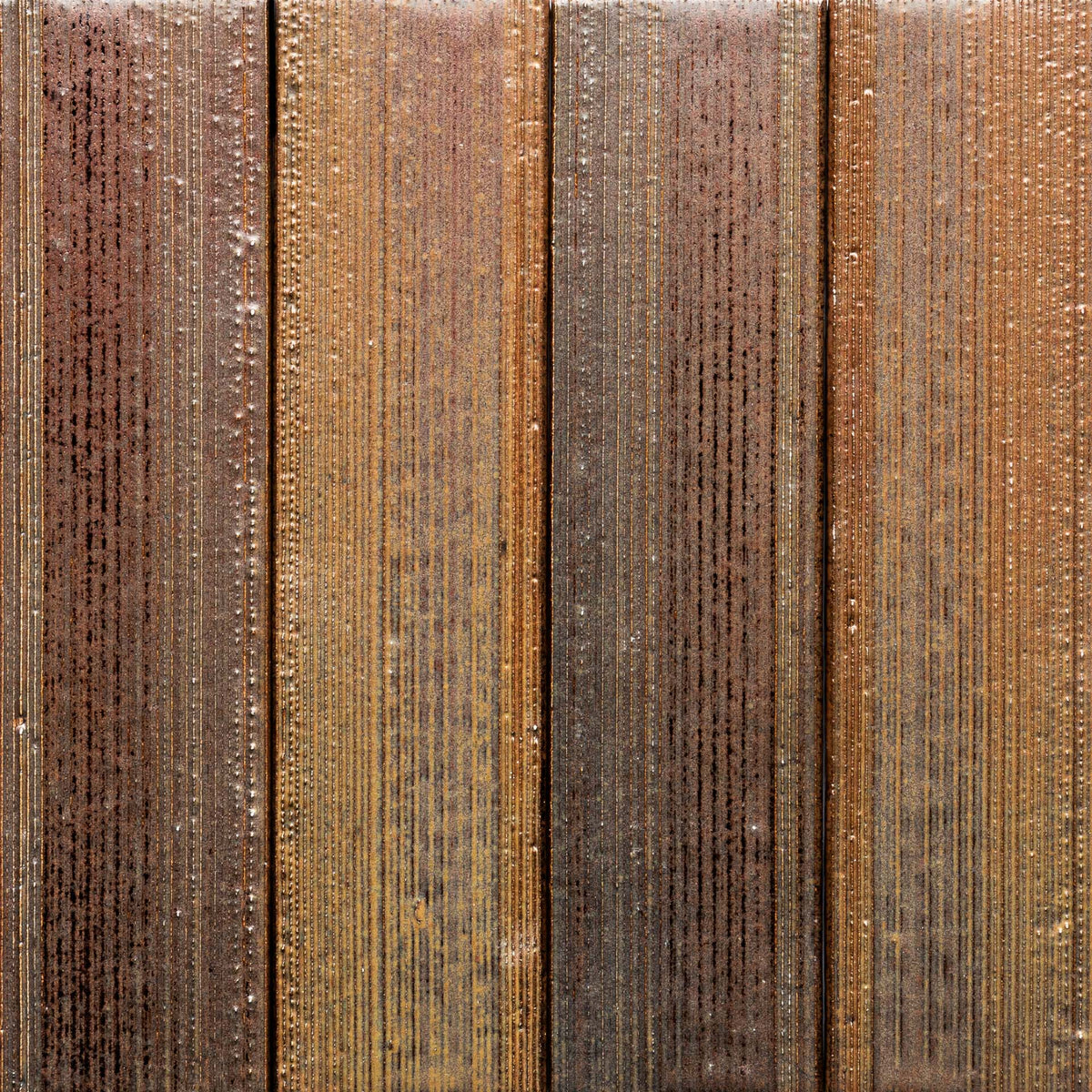Close-up of four vertical Buckeye + Etched, Sample panels by Zia Tile, featuring textured, striped patterns in various brown and tan hues with a wood-like appearance and visible moisture droplets.