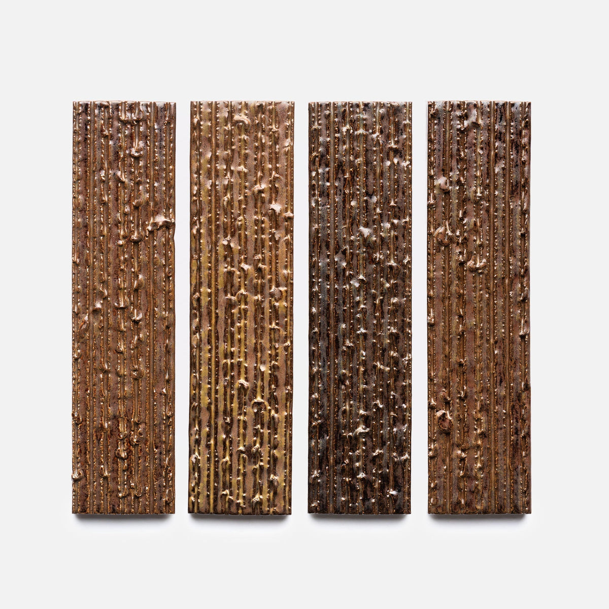Four Buckeye + Furrowed, Sample chocolate bars by Zia Tile in different brown hues, each featuring textured vertical lines and scattered bits, are arranged side by side on a white background.