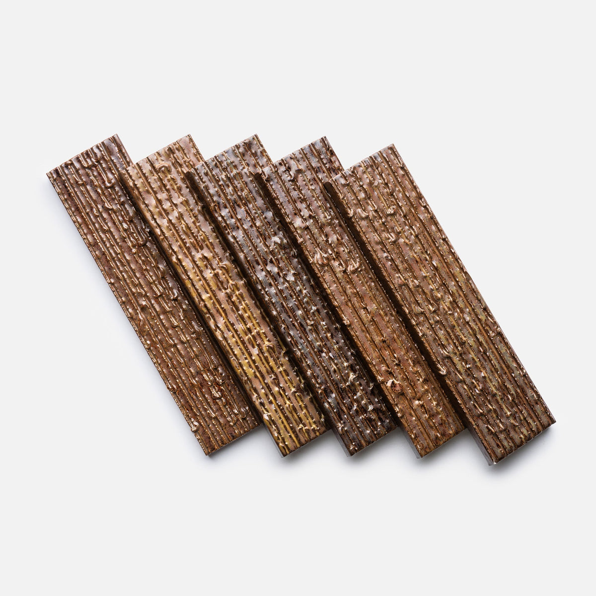 Five rectangular Buckeye + Furrowed, Sample tiles from Zia Tile are arranged diagonally on a plain white background. Each tile features a ridged texture and varies slightly in tone from light to dark brown.