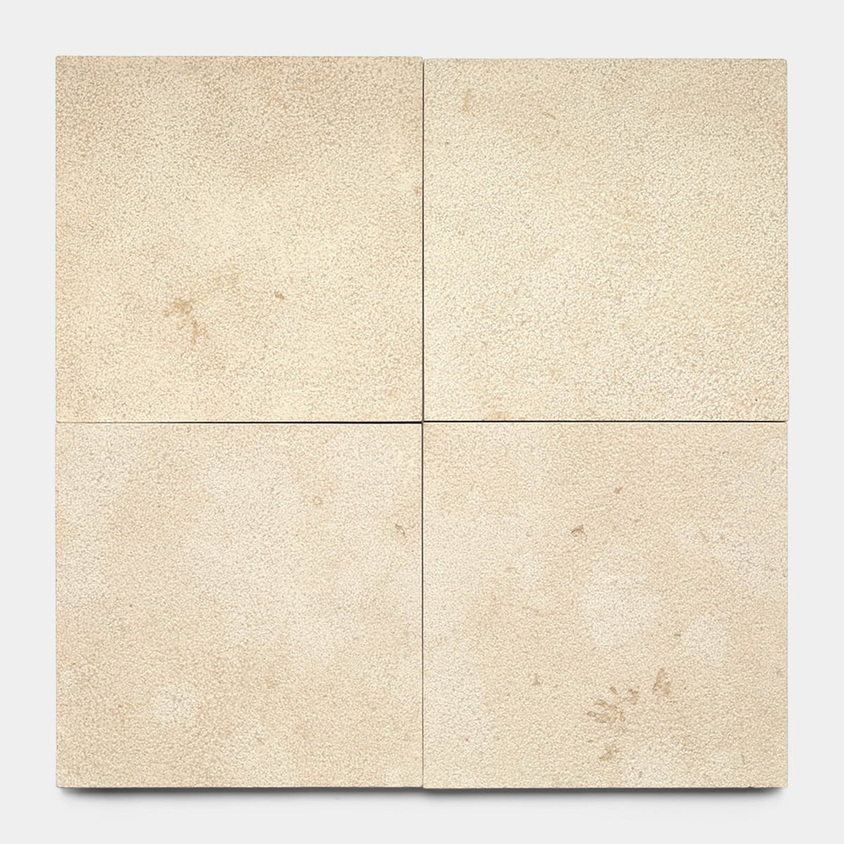 Four Buff 12x12 + Bush Hammered tiles by Zia Tile are arranged in a 2x2 grid, showcasing subtle texture and occasional small marks, all set against a plain white background.