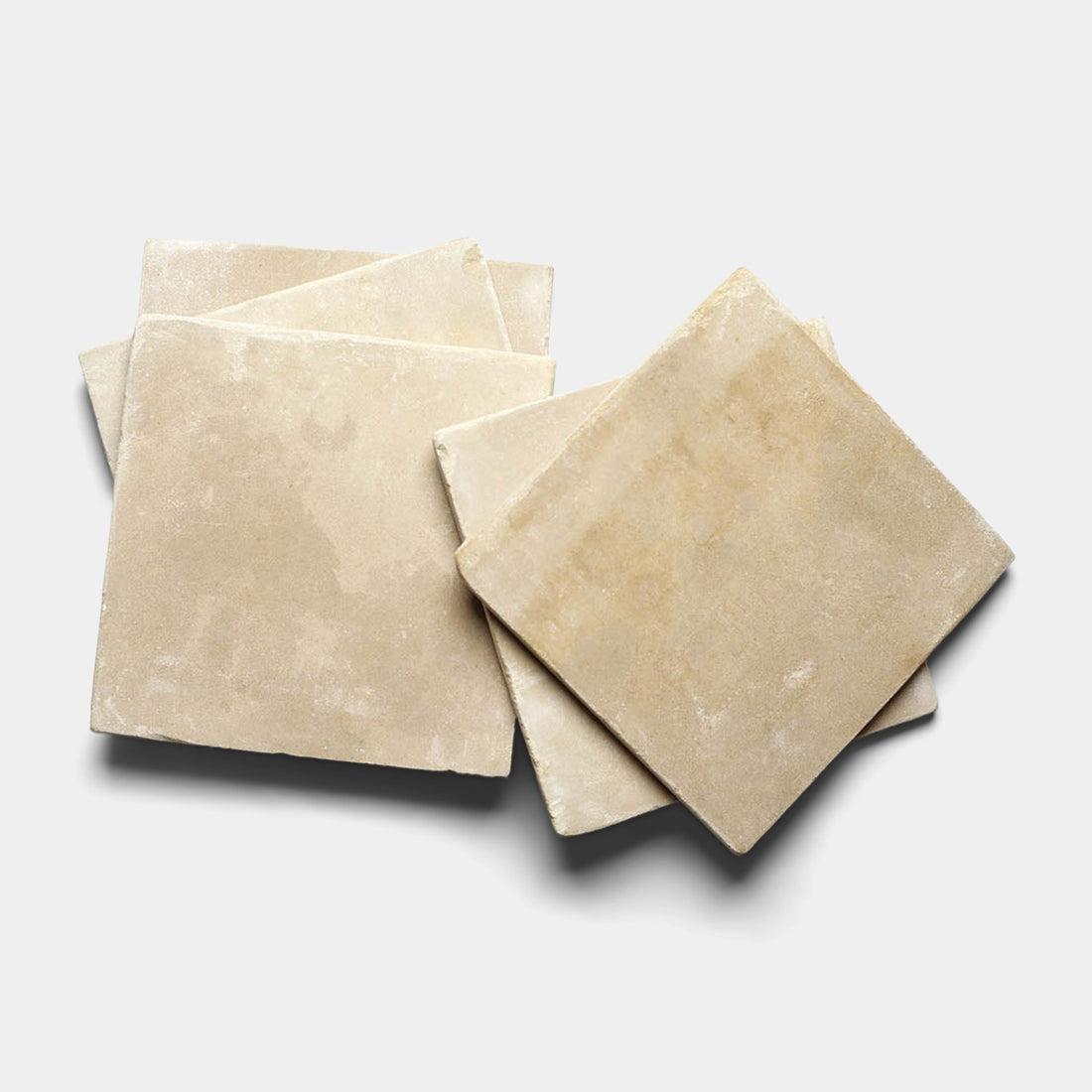 Four Buff 12x12 + Honed samples by Zia Tile, featuring matte beige surfaces and subtle color variations reminiscent of Moroccan Limestone, are stacked unevenly on a light gray background.