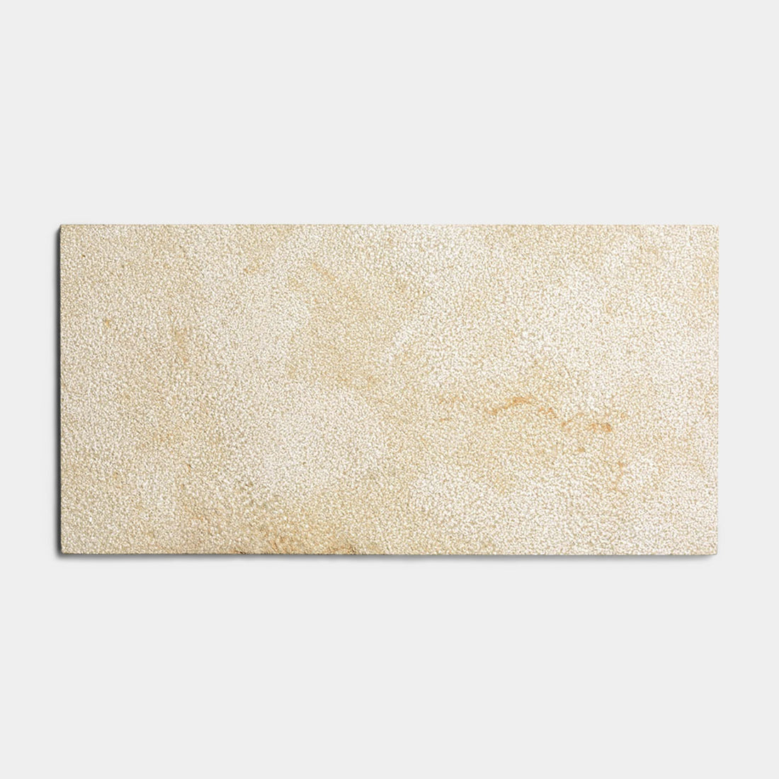 The Buff 12x24 + Bush Hammered tile sample by Zia Tile features a rectangular beige, Moroccan limestone-inspired design with a textured, speckled surface, shown against a plain light gray background.