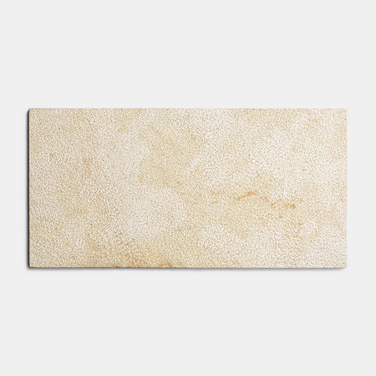 The Buff 12x24 + Bush Hammered tile sample by Zia Tile features a rectangular beige, Moroccan limestone-inspired design with a textured, speckled surface, shown against a plain light gray background.
