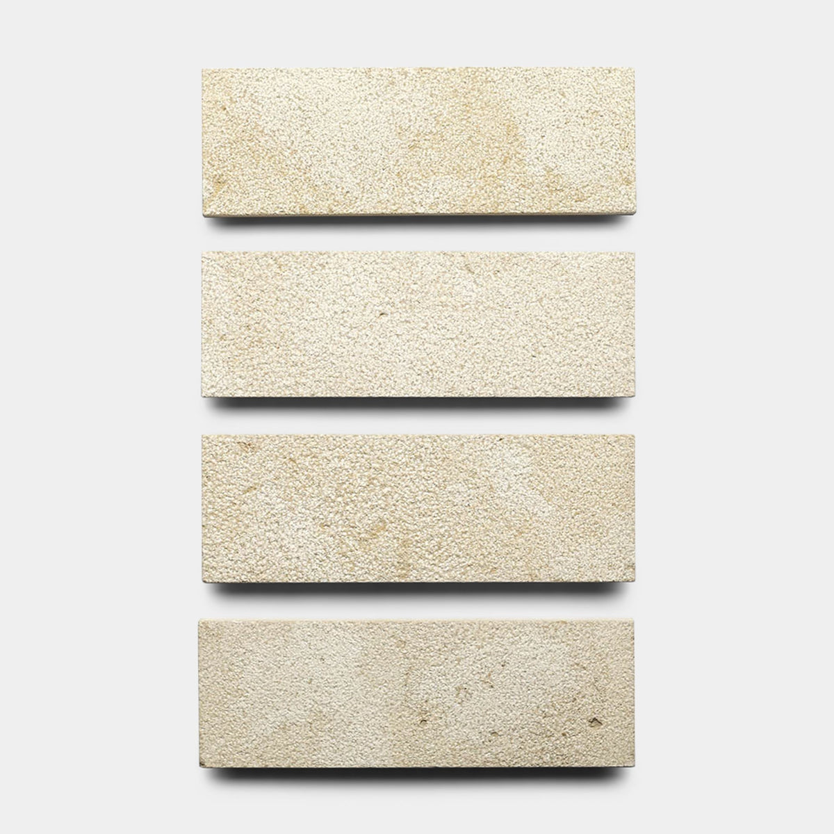 Four rectangular Buff 4x12 + Bush Hammered sample tiles by Zia Tile are arranged vertically in a single column on a plain, light gray background.