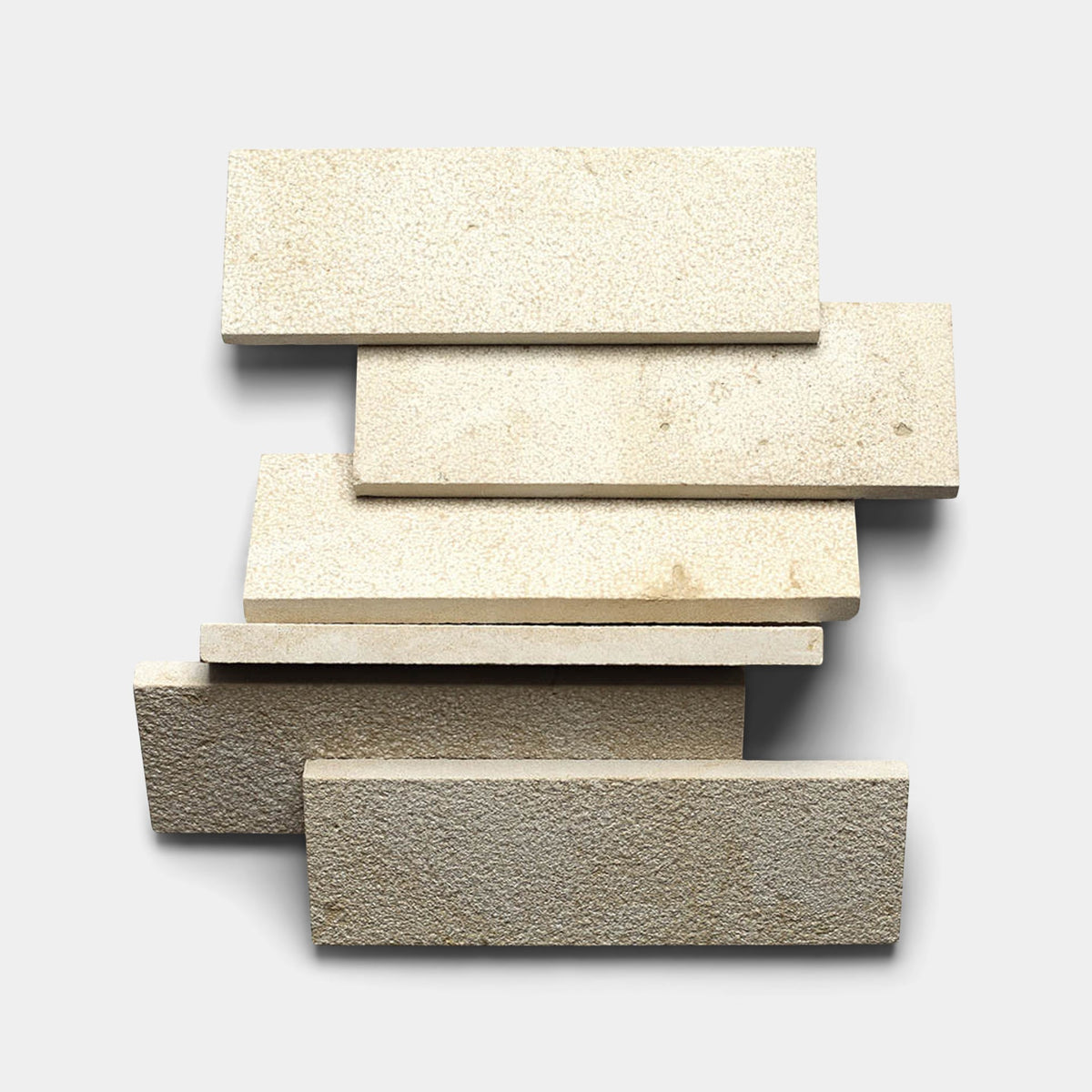 Five Buff 4x12 + Bush Hammered sample tiles by Zia Tile are arranged in a staggered, overlapping stack on a light gray background. The handmade surfaces create soft shadows, highlighting the tile’s textured finish.