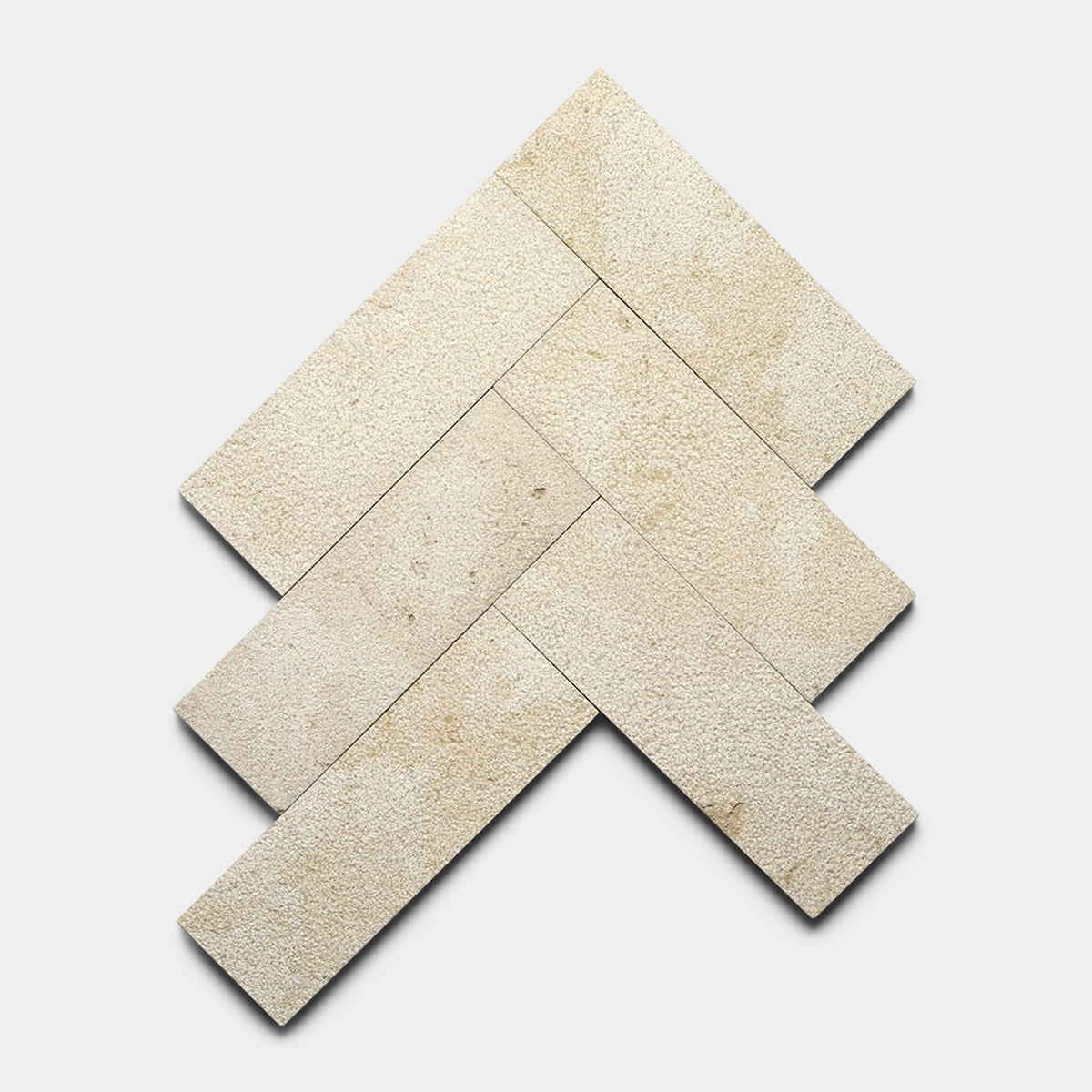 Five Buff 4x12 + Bush Hammered sample tiles by Zia Tile are arranged in a herringbone pattern on a white background, showing visible texture and subtle color variations.