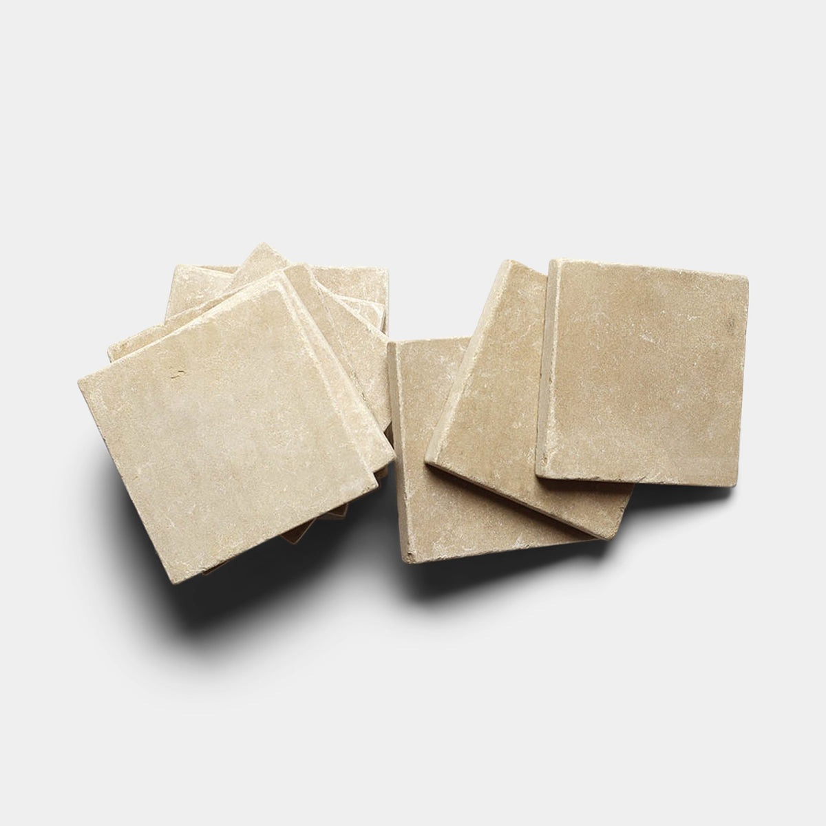 A group of Buff 6x6 + Honed, Sample tiles by Zia Tile are arranged in a slightly overlapping, irregular pile on a white background.