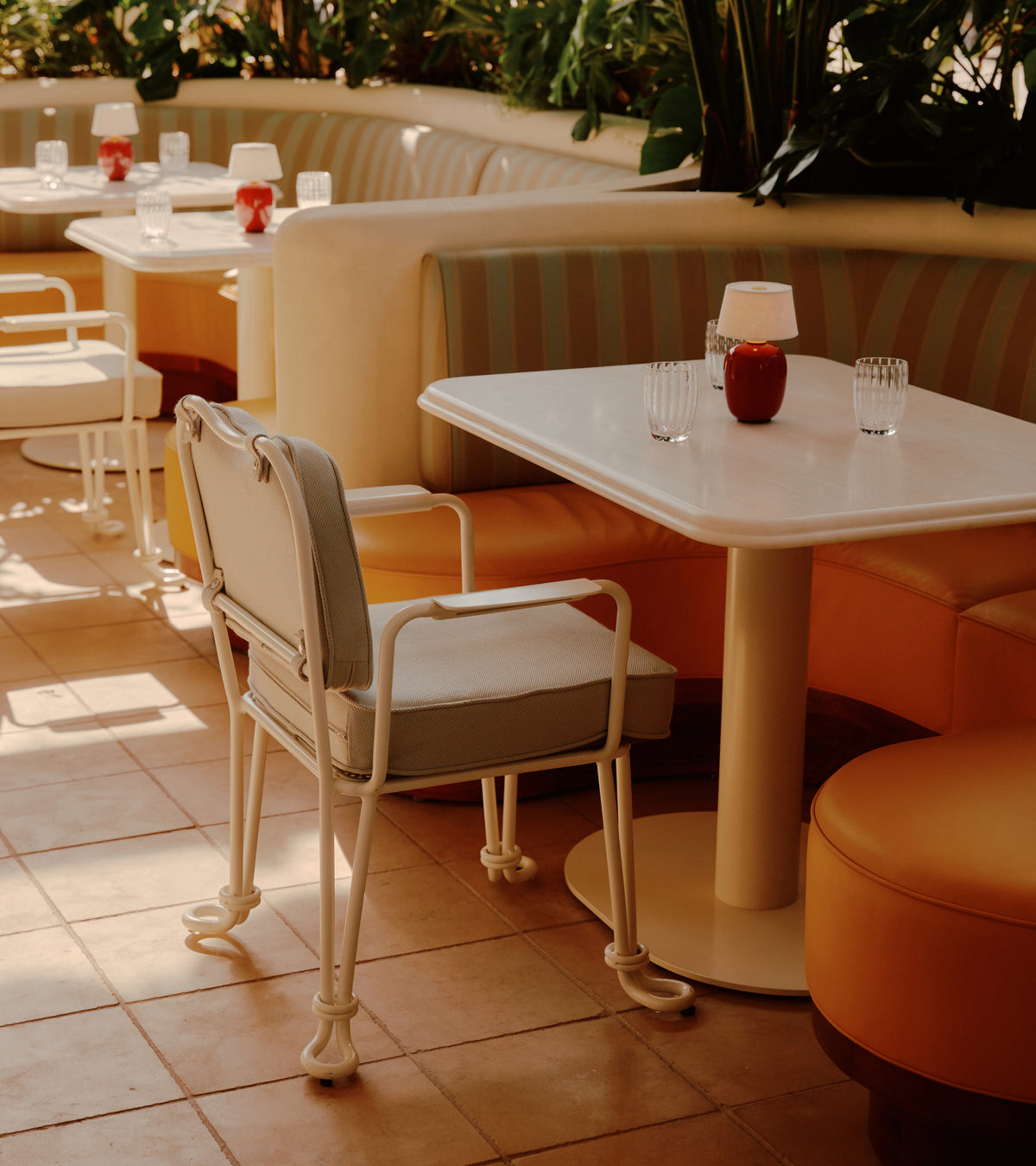 Tables with white tops, small red lamps, and chairs arranged on a floor of Buff 12x12 + Honed Moroccan limestone.