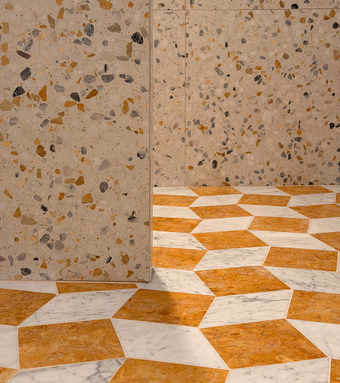 A beige terrazzo wall meets a geometric floor of Zia Tile’s Bungalow 12x12 brown and white cement tiles, forming a modern 3D cube pattern—perfect for decorative kitchen backsplashes or stylish cement flooring.