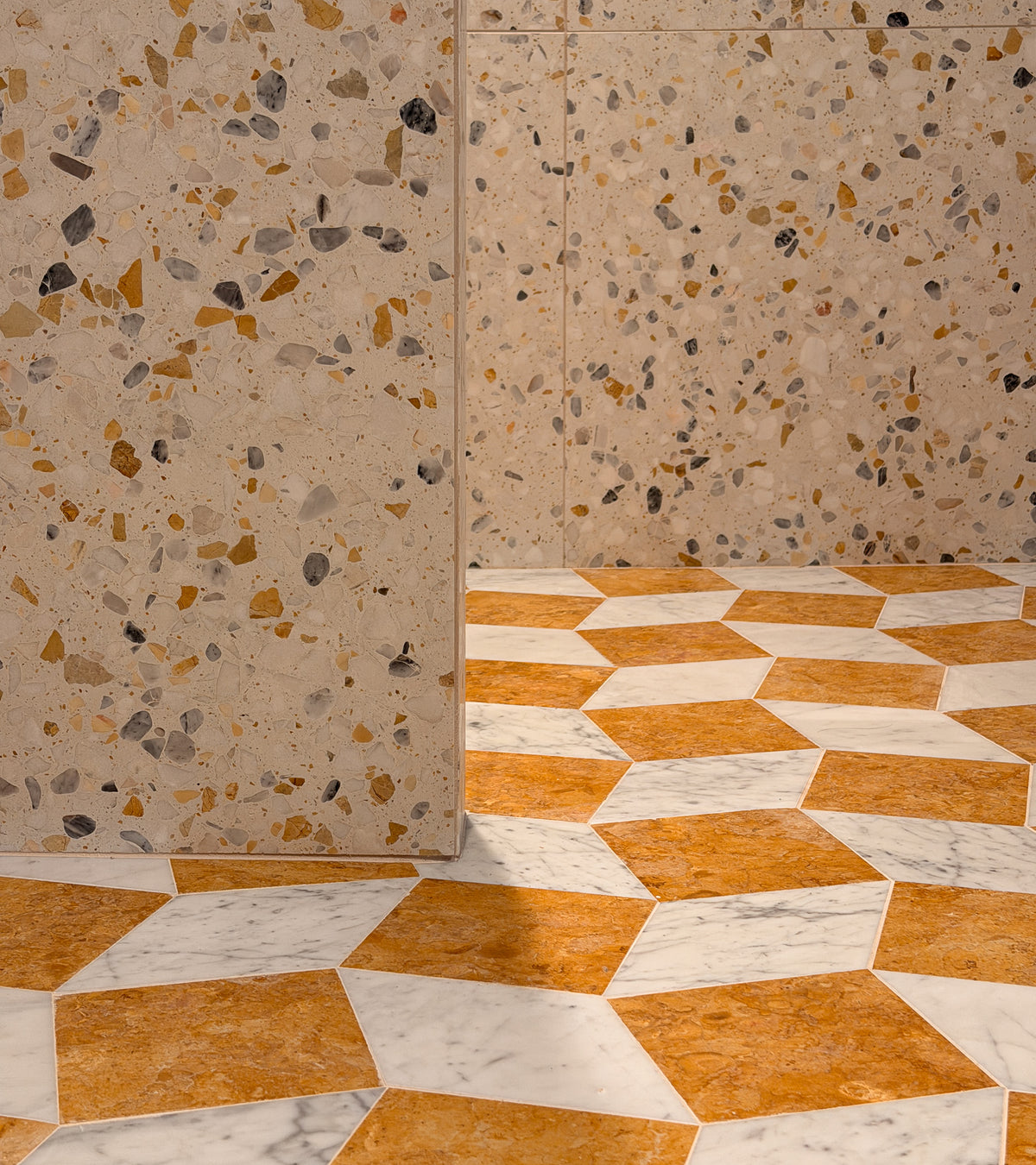 A beige terrazzo wall meets a geometric floor of Zia Tile’s Bungalow 12x12 brown and white cement tiles, forming a modern 3D cube pattern—perfect for decorative kitchen backsplashes or stylish cement flooring.
