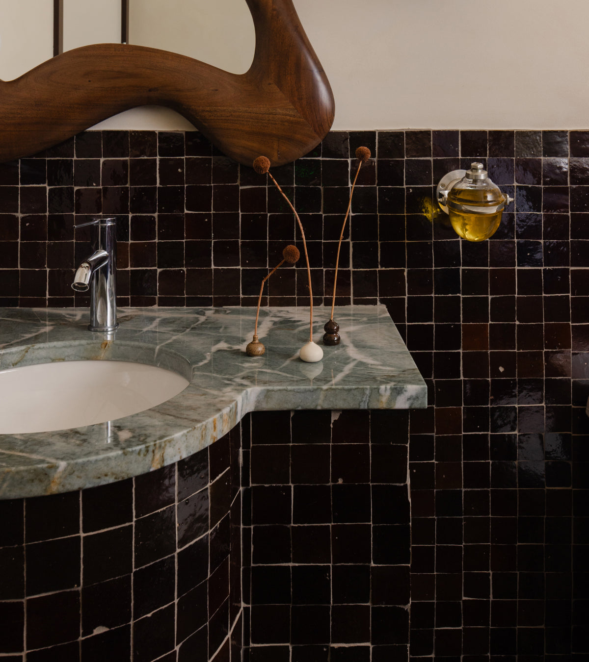 Bathroom wall covered in dark brown Burnt Sugar 2x2 zellige tiles behind a green marble vanity with a built-in sink.