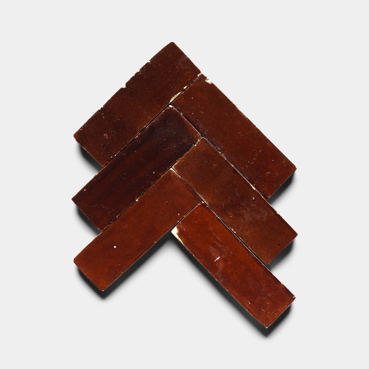 Five rectangular Burnt Sugar 2x6 tile samples from Zia Tile, arranged in a chevron pattern on a white background, resemble handcrafted designs.