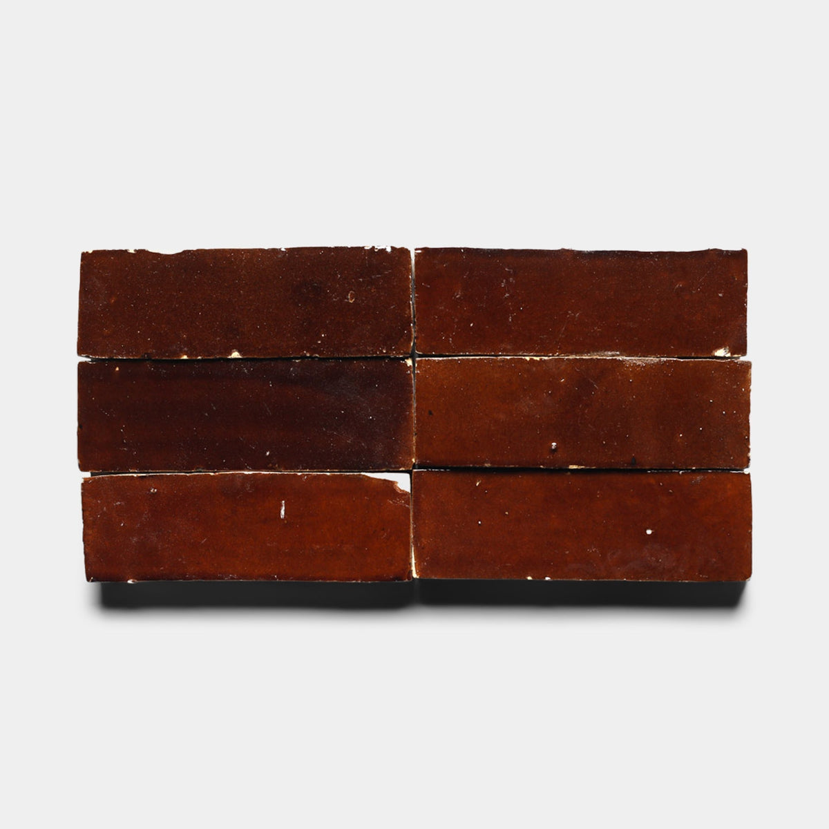 Six rectangular Burnt Sugar 2x6 tiles from Zia Tile, in a dark brown shade, are neatly arranged in two rows of three on a plain white background.