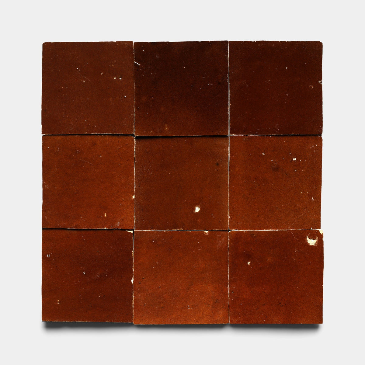 Nine Burnt Sugar 2x6 handcrafted tiles by Zia Tile are arranged in a 3x3 grid on a light gray background. The reddish-brown tiles feature small chips and color variations for a rustic, worn look. Sample shown.