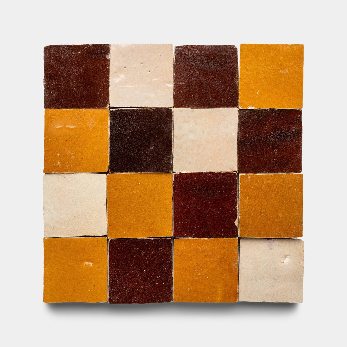 The Zia Tile Burnt Sugar + Glazed Earth + Amber Checkerboard Sample showcases sixteen handmade tiles in a 4x4 grid, alternating brown, cream, and yellow tones on a white background.