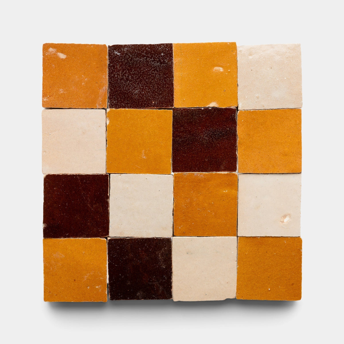 The Burnt Sugar + Glazed Earth + Amber Checkerboard Sample from Zia Tile features 16 handmade tiles in a 4x4 grid, alternating rich brown, mustard yellow, and off-white shades for a bold checkerboard effect.