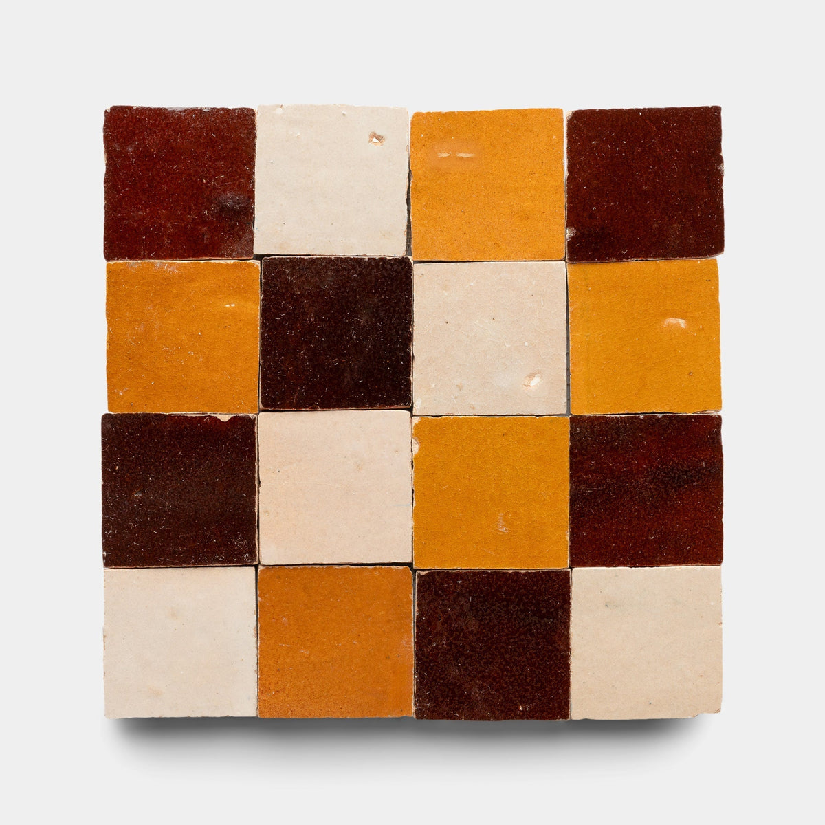A 4x4 square grid of 16 handmade tiles in dark red, mustard yellow, and off-white shades—ideal for Zia Tile fans. Product: Burnt Sugar + Glazed Earth + Amber Checkerboard Sample by Zia Tile.