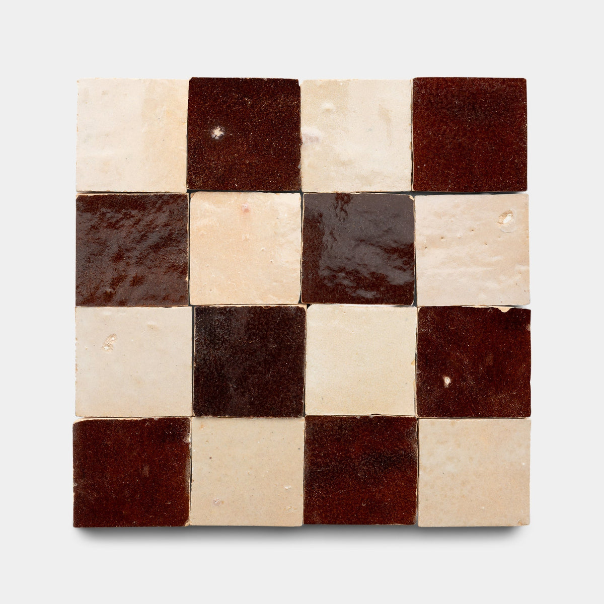 A 4x4 square of Zia Tile's Burnt Sugar + Glazed Earth Checkerboard Sample features 16 glossy ceramic tiles in alternating dark brown and cream, arranged on a plain white background.